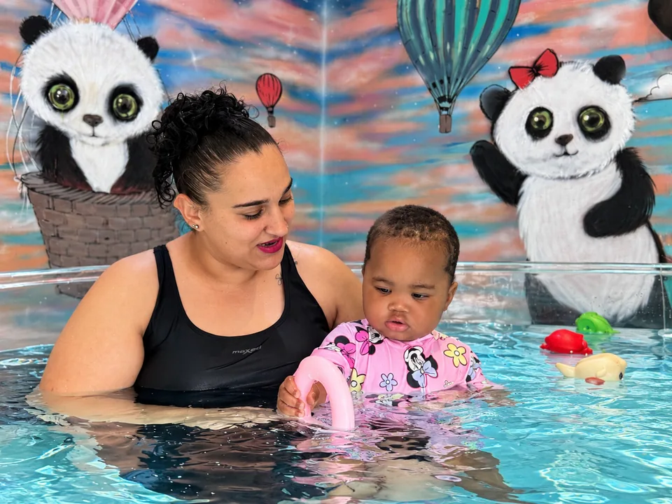 An instructor supporting a baby exploring a pink water toy in the round pool